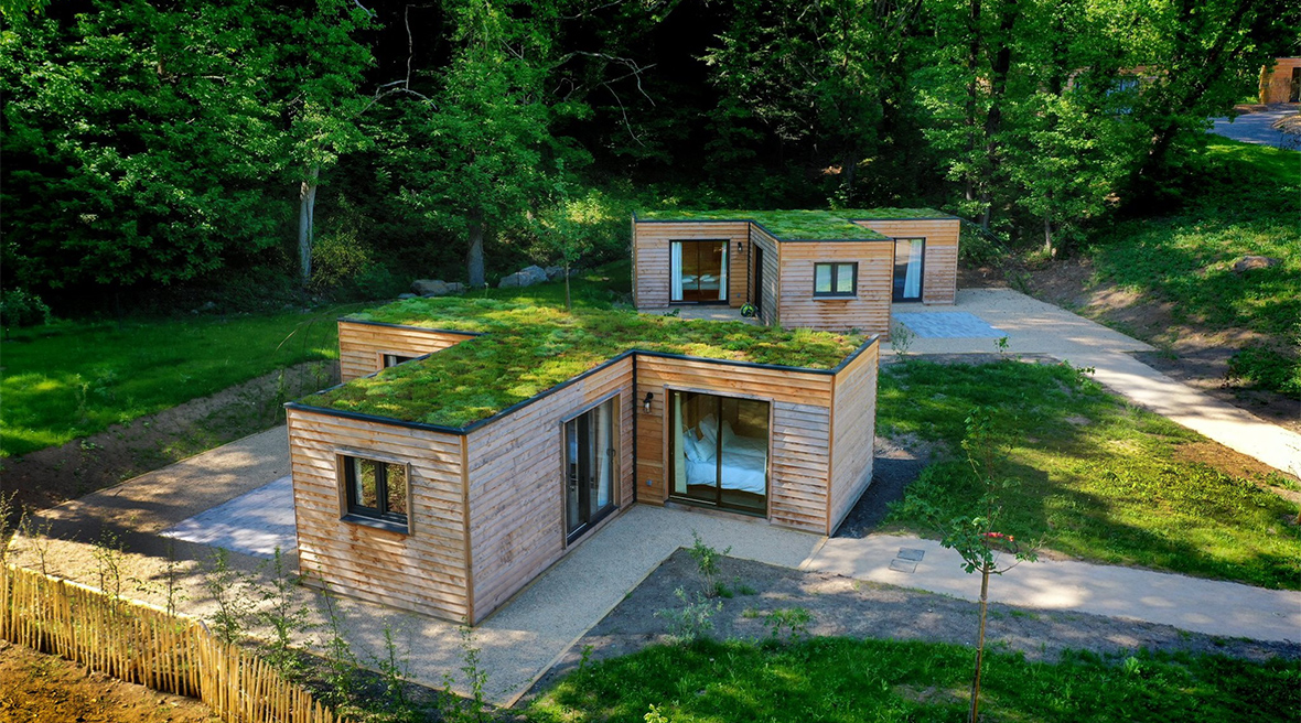 A drone view of two wooden T-shaped lodges with grass roofs